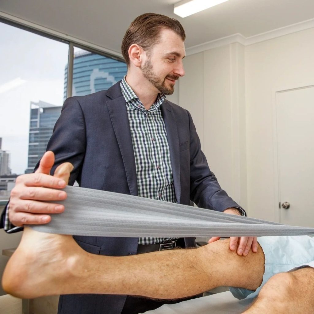 Dr Alexey Borshch guiding ankle and Achilles rehabilitation exercises with a resistance band