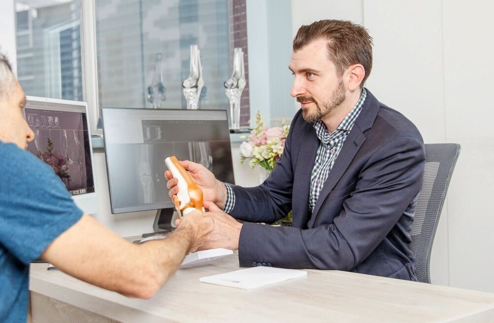 Doctor Alexey Borshch explaining knee replacement surgery to patient in consultation.